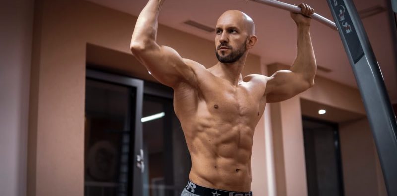 A bald, muscular man performing exercise on gym equipment indoors.